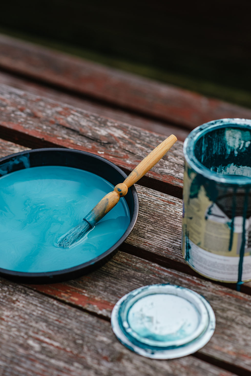 A paint can with teal paint and a paint brush