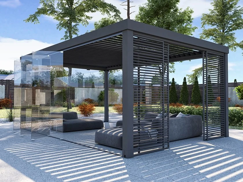A metal pergola with a cream fabric roof in a sunny outdoor area, the pergola covers a comfy seat against a white wall, with bright blue cushions and trees surrounding it.